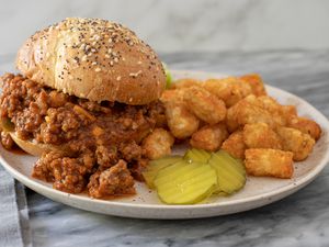 sloppy joe sandwiches with pickles and tater tots on a plate