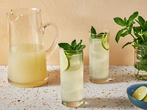 A pitcher of Mojito with two glasses of mojito garnished with lime wheels and fresh mint