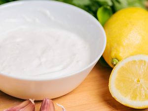 Yogurt garlic sauce in a bowl alongside lemons, garlic cloves, and herbs