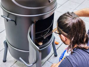 A person places meat inside the Char-Broil Bullet Charcoal Smoker, 20-Inch