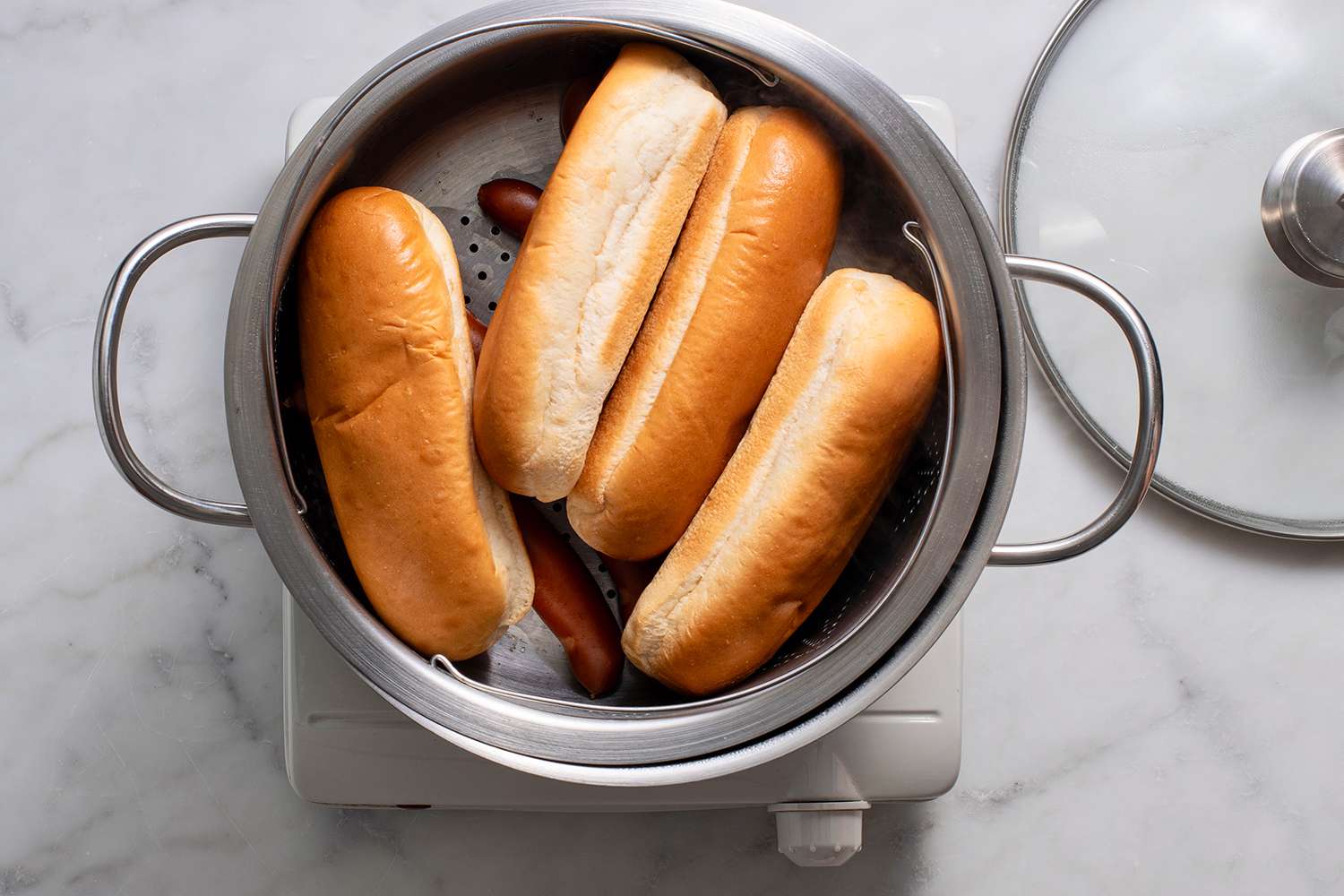 Hot dogs and buns in a steamer basket