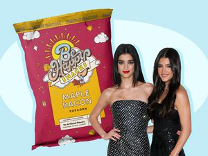 A bag of "Be Happy" brand popcorn, maple bacon flavor, next to a photo of the D'Amelio sisters