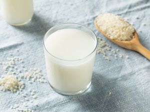 A glass of rice milk next to a wooden spoon filled with raw rice grains