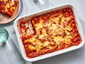 A ravioli lasagna in a baking dish, with a serving removed and served on a pink plate