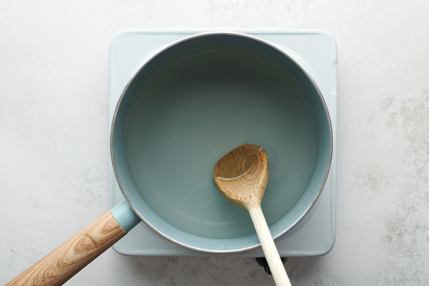 A pot of water and sugar, being stirred with a wooden spoon