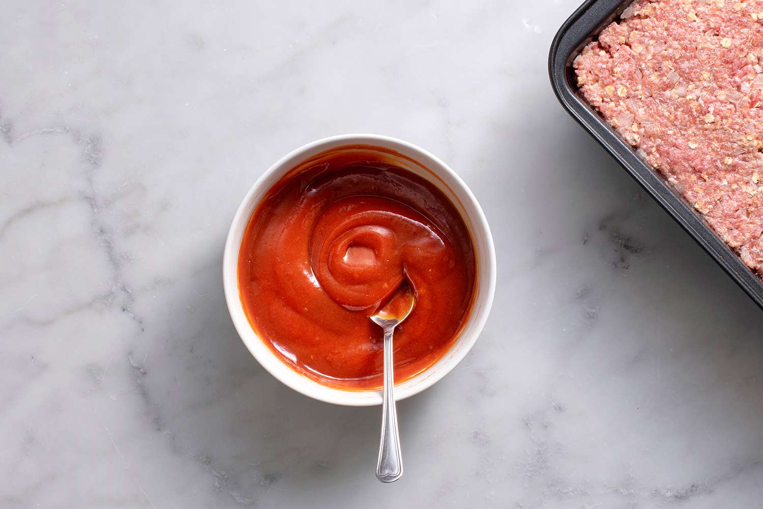 Ketchup, brown sugar, and mustard being stirred in a small bowl with a spoon