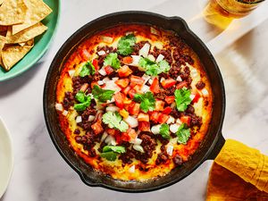 A cast iron skillet with choriqueso topped with diced onions, tomatoes, and cilantro, and served with pita chips