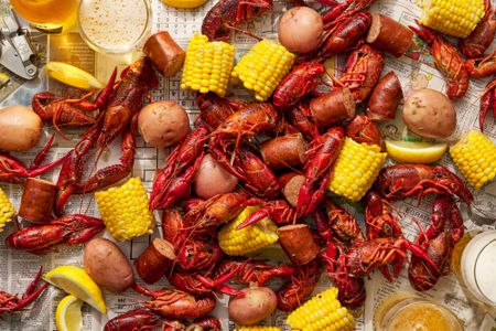 Boiled crawfish, sausage, potatoes, and corn laid out in a newspaper, served with lemon wedges and beer