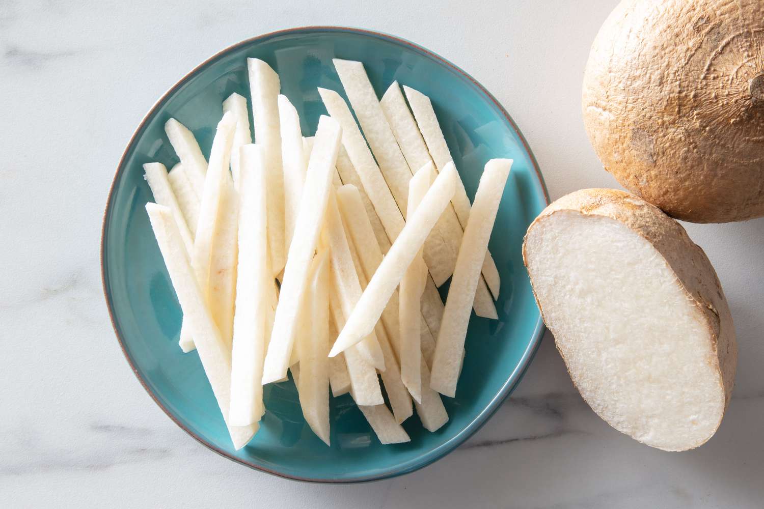 A small plate of matchstick-cut jicama, with a half and whole jicama in frame