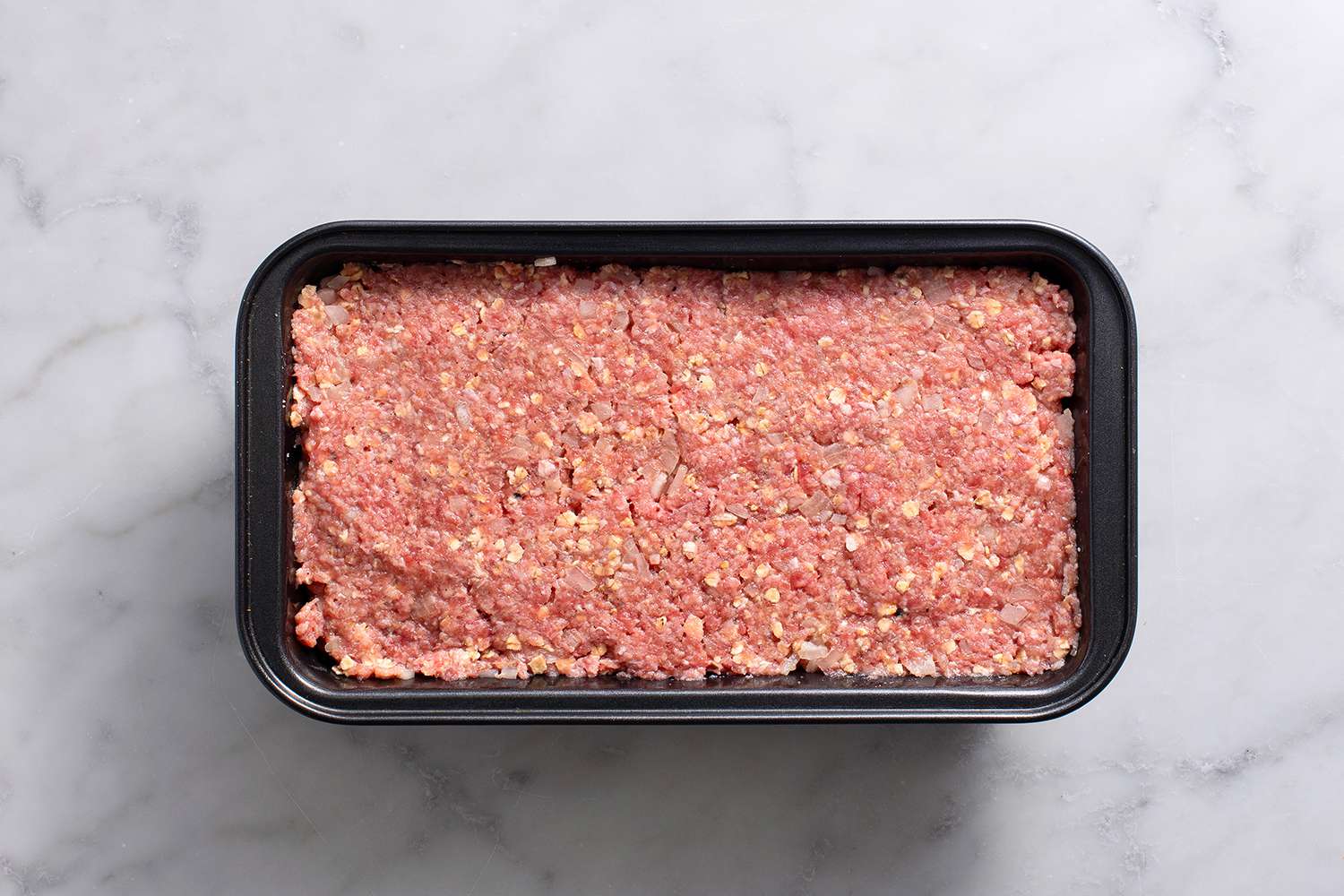 Raw meatloaf mixture filled into loaf pan with the top leveled and smoothed