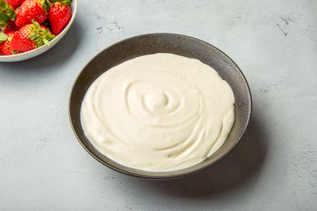 A bowl of homemade creme fraiche with strawberries in the background