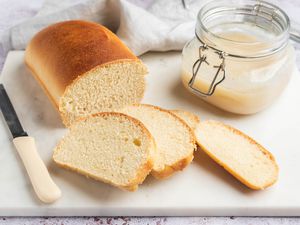 Potato flake sourdough bread sliced on a cutting board with a starter in a jar