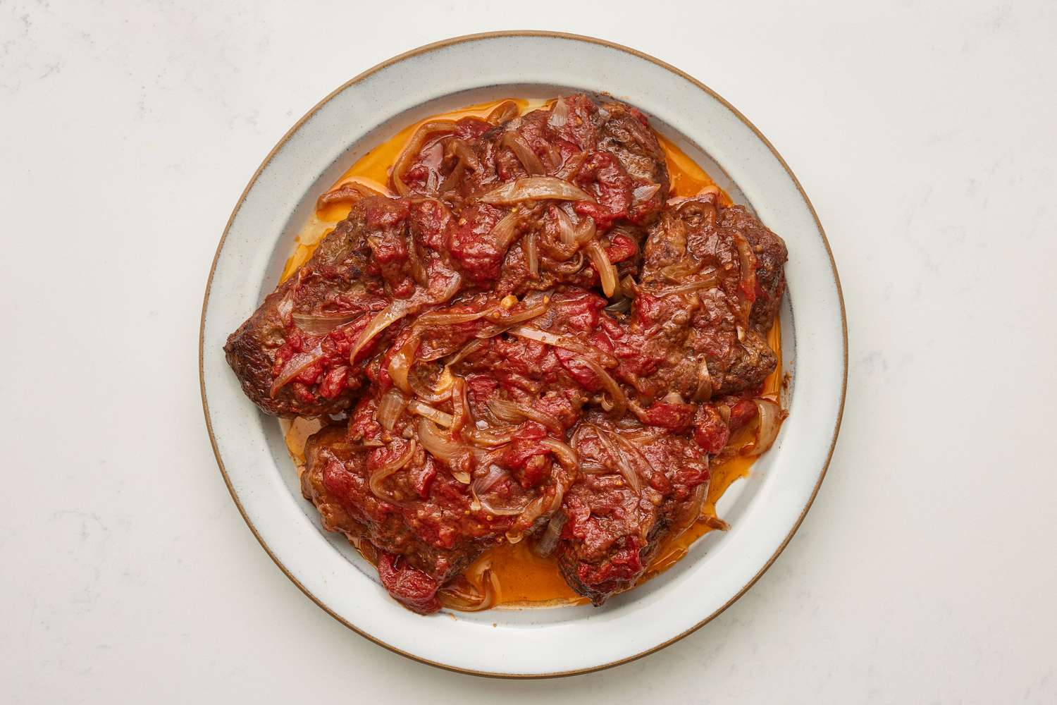 A plate of swiss steak topped with onion-tomato sauce