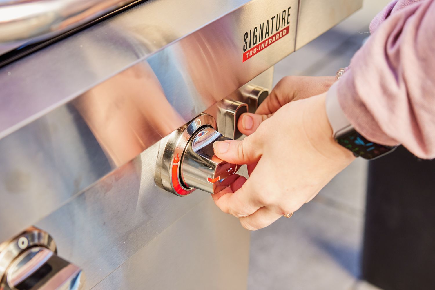 Hands turning a knob and pressing a button on the Char-Broil Signature Series Amplifire 2-Burner Gas Grill
