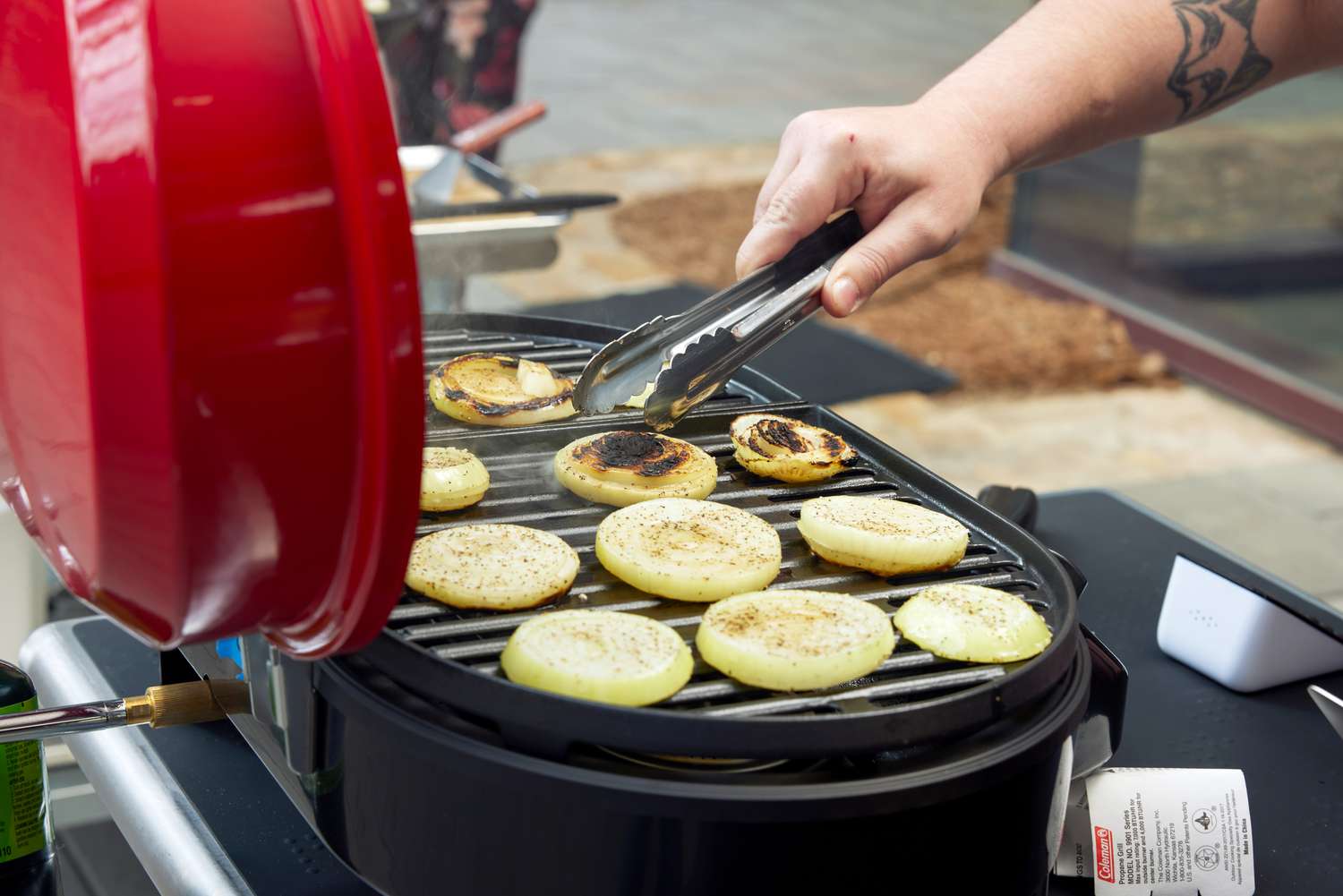 A man grills onions on a Coleman Roadtrip portable grill