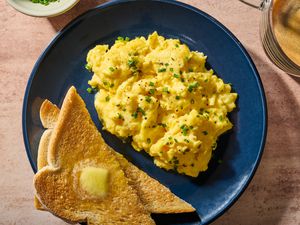 A plate of scrambled eggs, topped with chopped chives, served with toast and butter