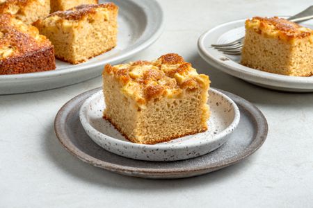 A slice of apple snacking cake with a platter of apple snacking cake