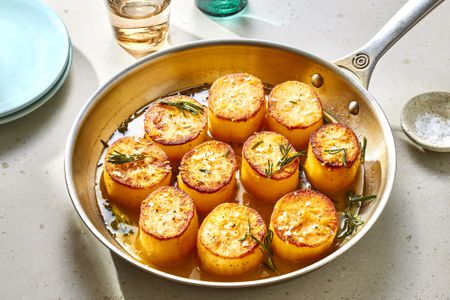 A skillet with fondant potatoes, topped with fresh herbs