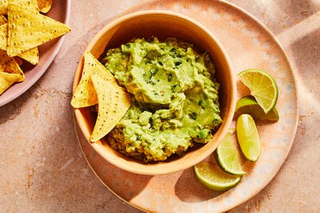 A bowl of guacamole, served with tortilla chips and lime wedges