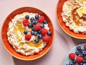 Two bowls of traditional Scottish porridge, with one topped with fresh berries and syrup, and one topped with butter and cinnamon