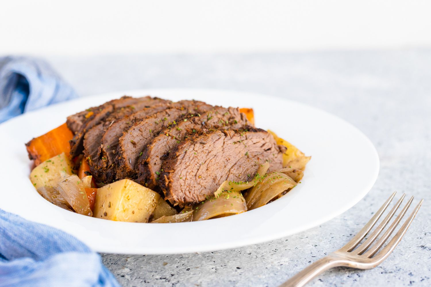 Thick slices of tri-tip roast served over vegetables on a deep dinner plate