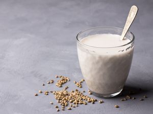 A glass of hemp milk with a spoon sticking up in the glass and hemp seed scattered around the base of the glass