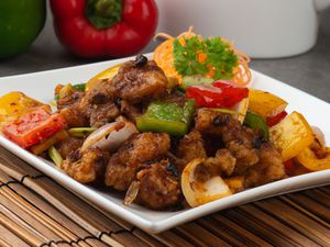 Plate of fish filet and vegetables topped with garnish which happens to be cilantro. There are peppers in the background and the the plate is a ceramic white plate.