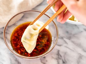 Dumpling dipping sauce in a glass bowl with a dumpling secured with chopsticks