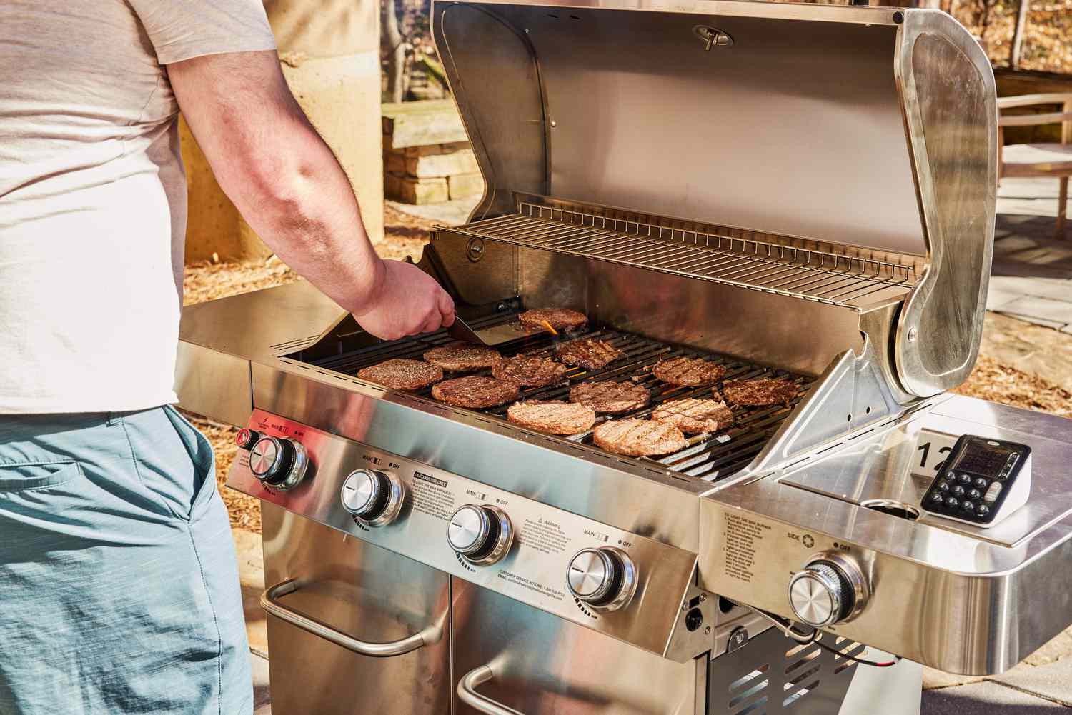 Person grilling patties on the Monument Grills Stainless 4-Burner Propane Gas Grill