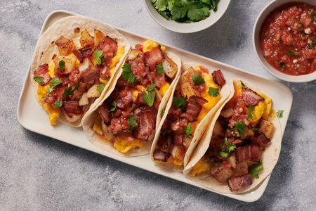A small platter of Tex Mex breakfast tacos, served with extra cilantro and salsa on the side.