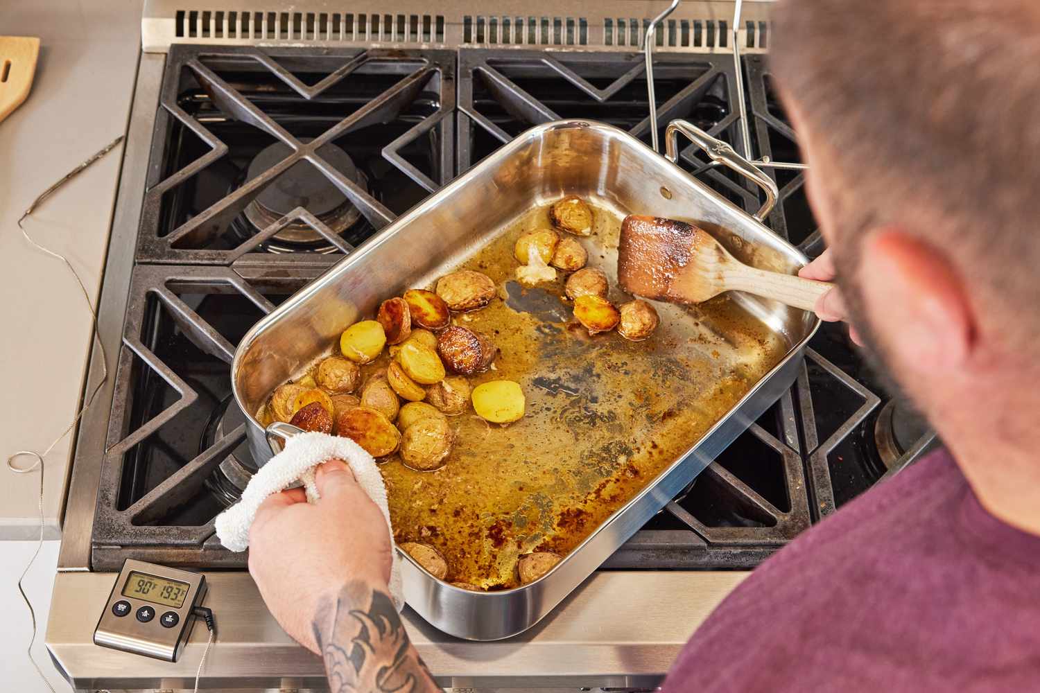 Person holding a spatula and the Hestan Provisions Stainless Steel Classic Roaster with Rack full of potatoes