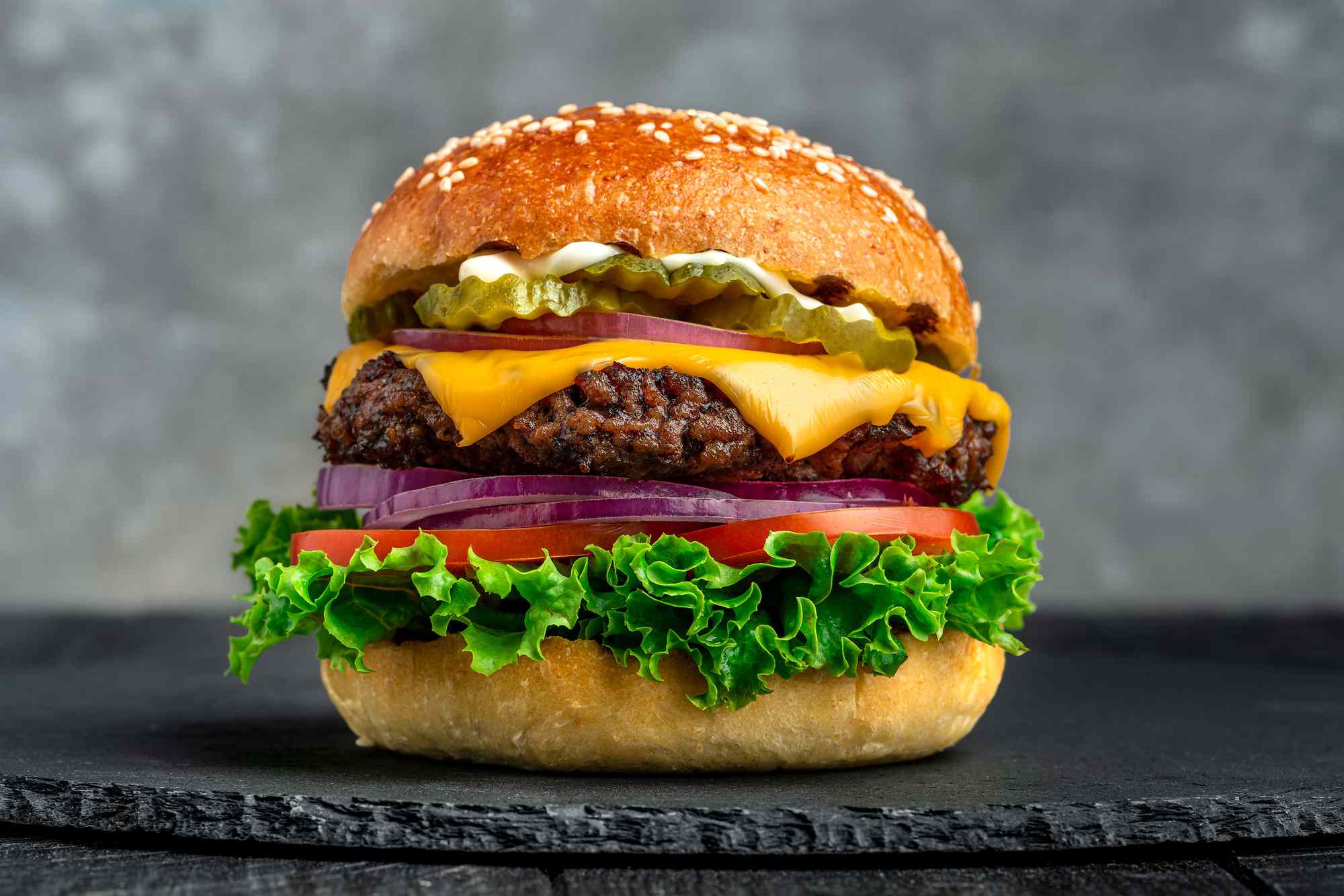 A grilled cheese burger topped with cheese, pickles, lettuce, tomato, and onion