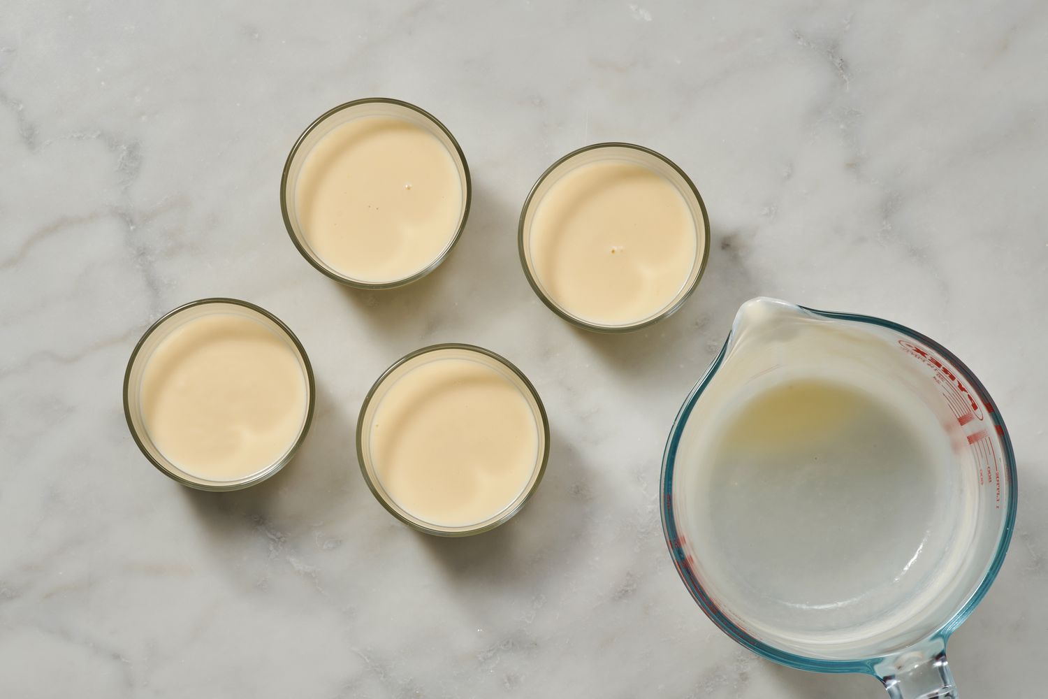 An empty glass measuring cups with four glasses filled with lemon posset