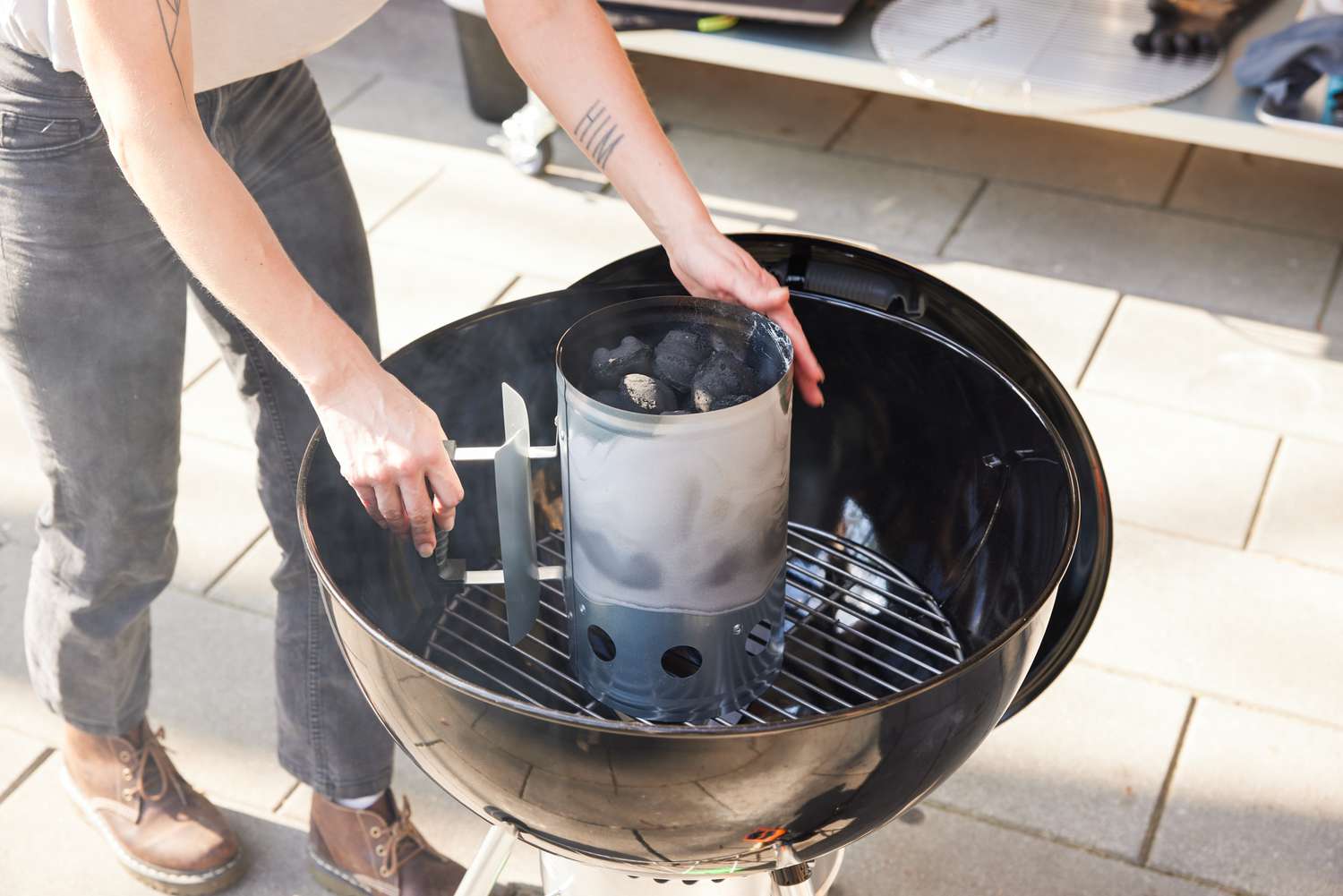 Hands pouring hot coals into a Weber Original Kettle Premium 22-Inch Charcoal Grill