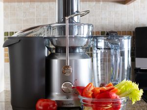 Breville Juice Fountain Cold Electric Juicer displayed on marble countertop with nearby tomato, red pepper, and celery