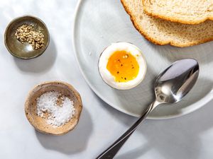 A soft boiled egg, served with extra salt and pepper and two pieces of bread