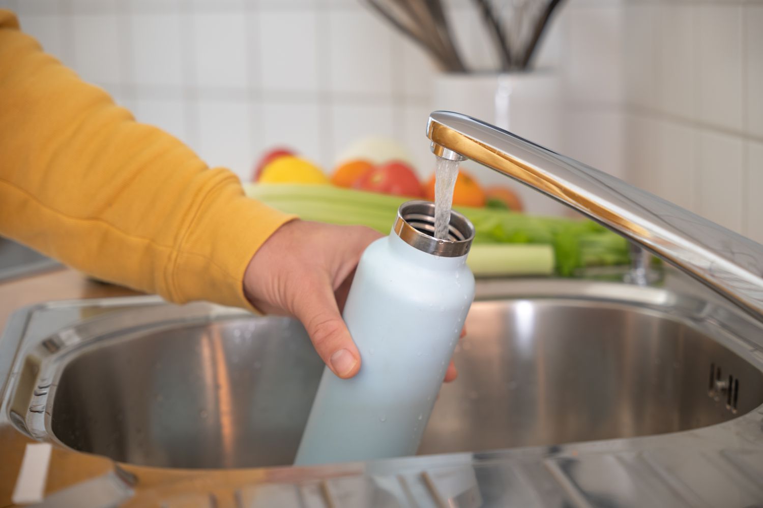 A person holding a blue water bottle next to a running faucet 