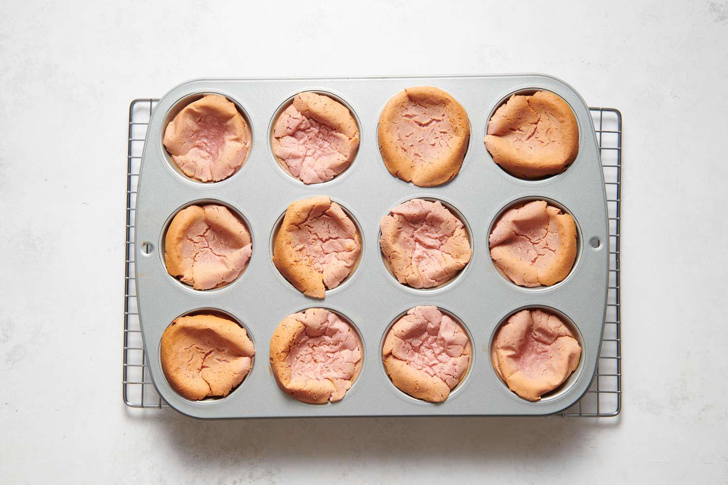 A muffin pan of baked strawberry miso mochi muffins sitting on a cooling rack