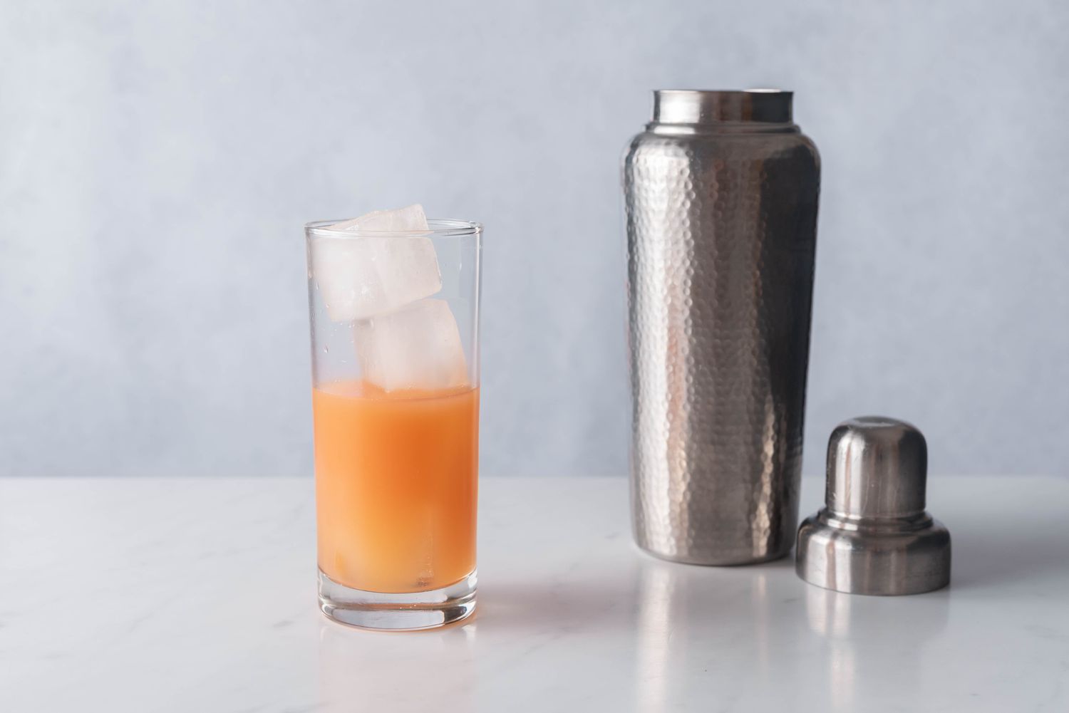 Cocktail shaker next to a chilled Collins glass filled with strained Cinderella mocktail ingredients