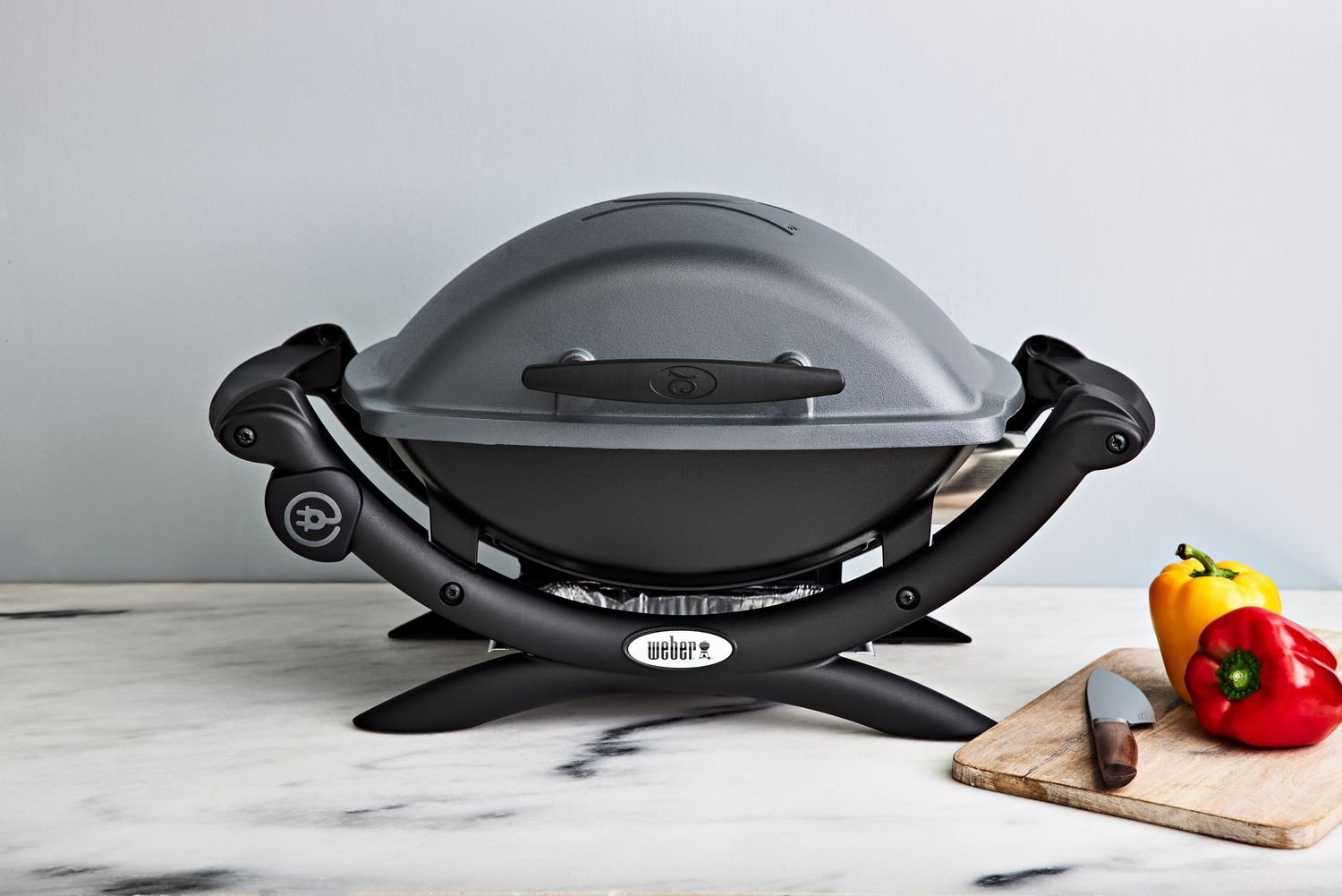 Weber Q 1400 Electric Grill on a counter near a cutting board, knife, and bell peppers