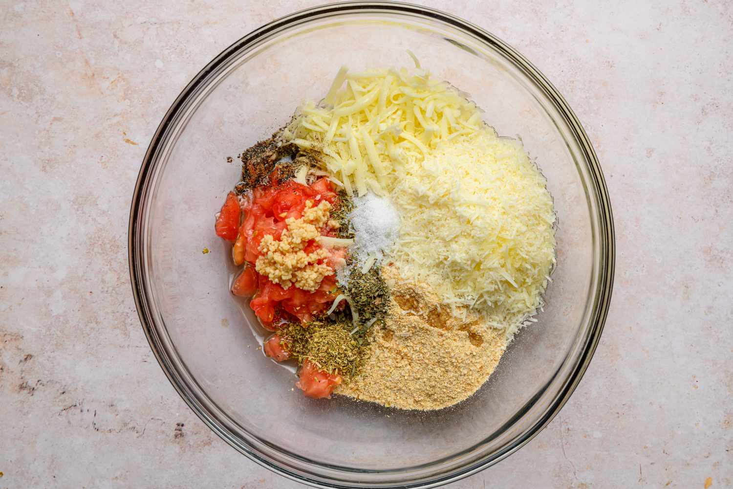 A large bowl with tomato scraps, breadcrumbs, Parmesan cheese, mozzarella cheese, garlic, herbs, salt, pepper, and olive oil