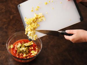 scraping corn off of a plastic cutting board into a bowl