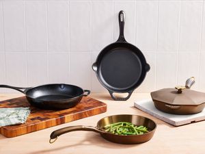 Assortment of cast iron skillets we recommend displayed on cutting boards and a wooden surface against a tiled background 