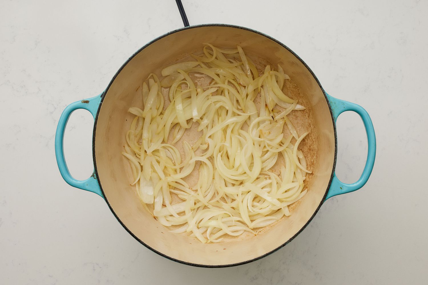 A large dutch oven with sliced onions cooking in oil