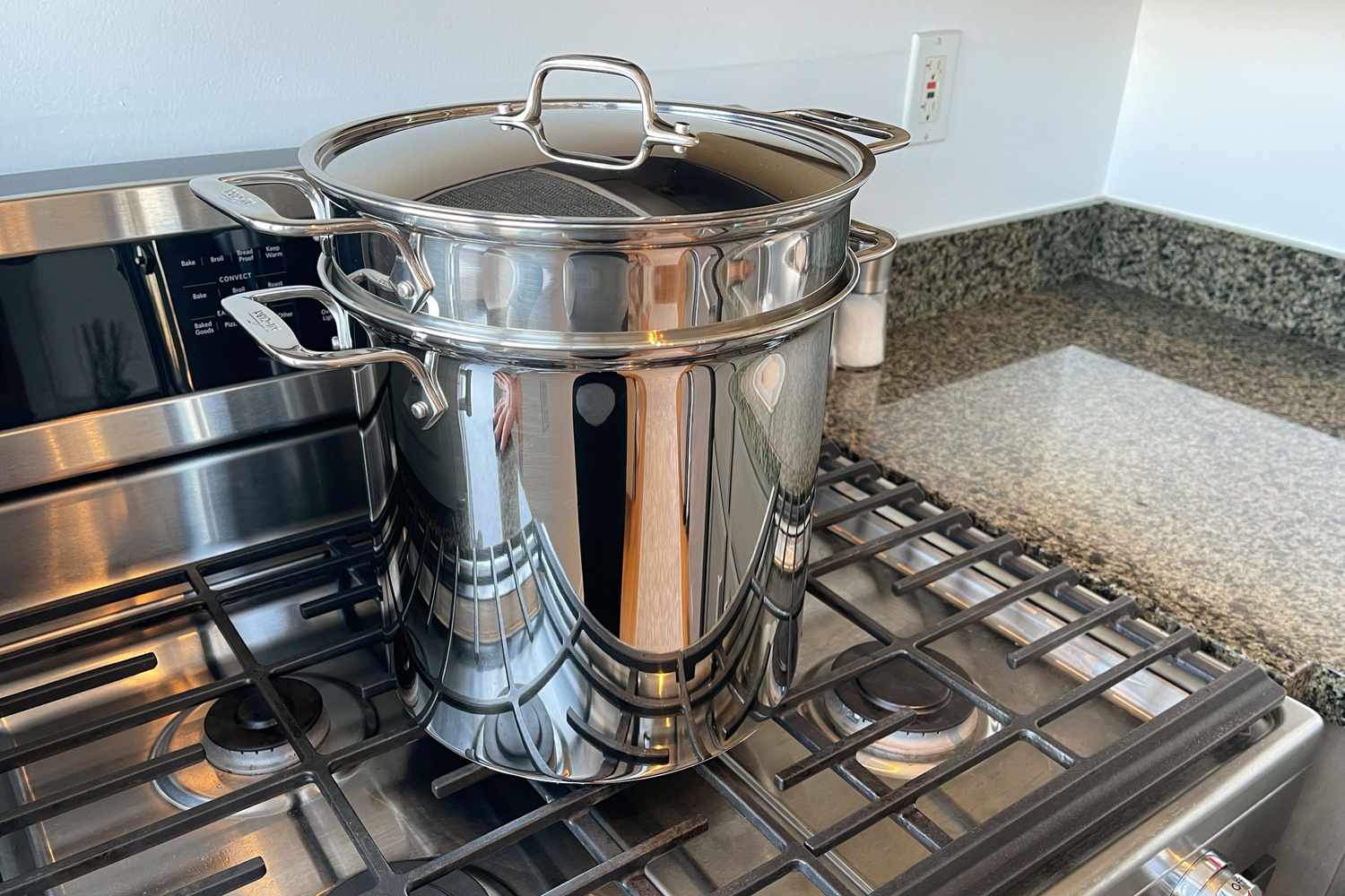 The All-Clad Gourmet Accessories Stainless Steel Multi-Pot with Perforated Steamer Insert and Lid, 12 Quart sits on the stovetop