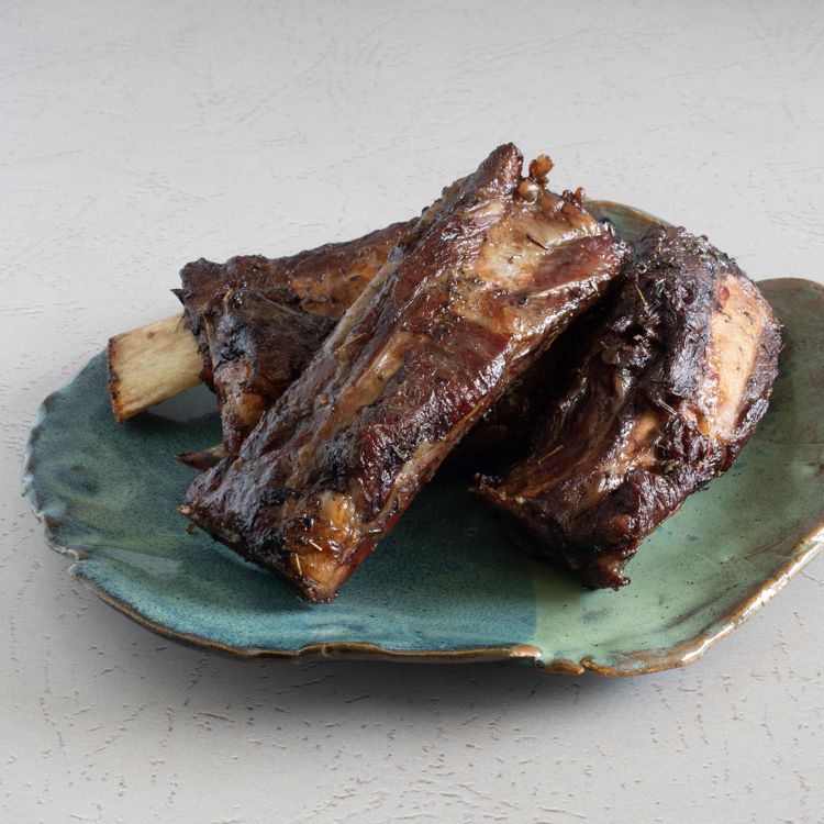Tender slow-grilled beef ribs stacked on a plate