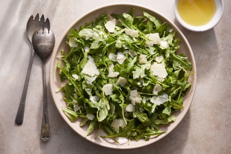 A large bowl of arugula salad, topped with shaved parmesan cheese and served with lemon vinaigrette