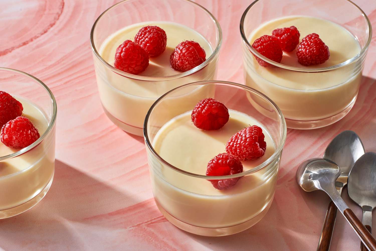 Four servings of lemon posset in glass cups, garnished with fresh raspberies