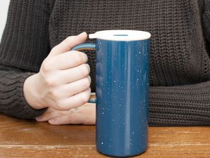 Hand holding Ello Campy Stainless Steel Travel Mug displayed on wood table