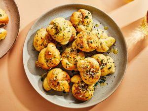 A large plate of garlic knots topped with garlic and herbs